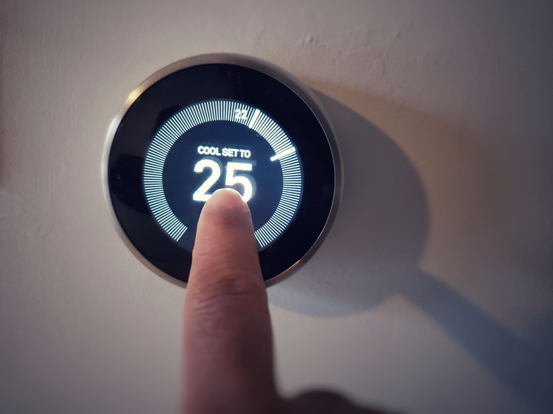 A women hand adjusting the temperature on circle Thermostat -  Wireless Learning in dark blurred background